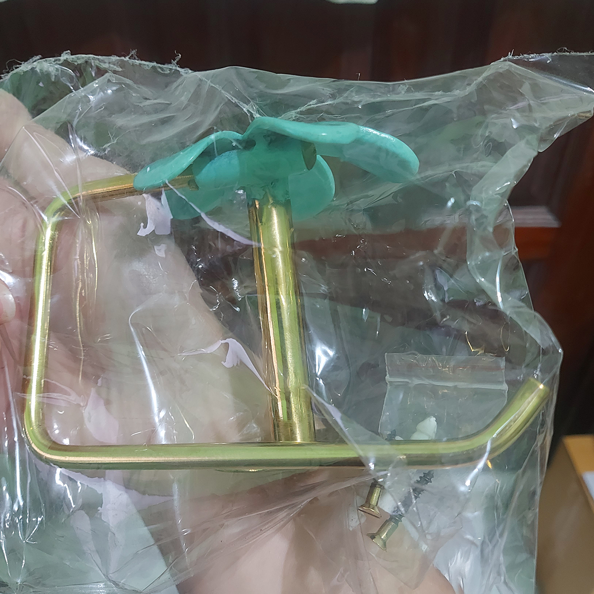 Packaged brass toilet paper holder showing open-ended roll arm